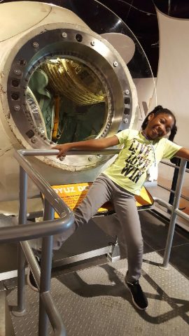 Smiling student posing beside a Soyuz space capsule exhibit