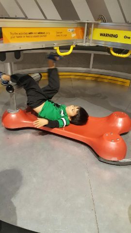 Student lying on a spinning platform at a hands-on physics exhibit