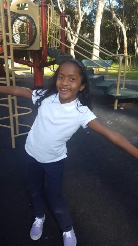 Student in a school uniform smiling with arms outstretched on a playground