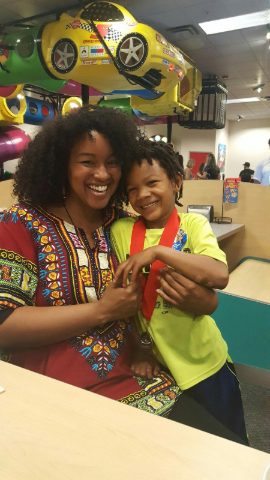 Smiling adult in a colorful patterned shirt hugging a student who is wearing a medal