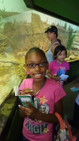 Student writing in a notebook beside a desert habitat exhibit at a museum